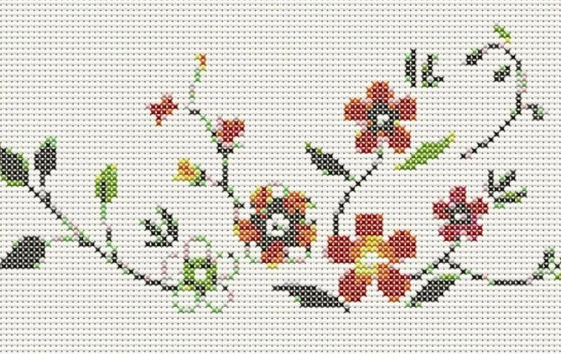 Une main tient un tambour à broder en bois avec une petite broderie florale en point de croix, échevette de coton et ciseaux
