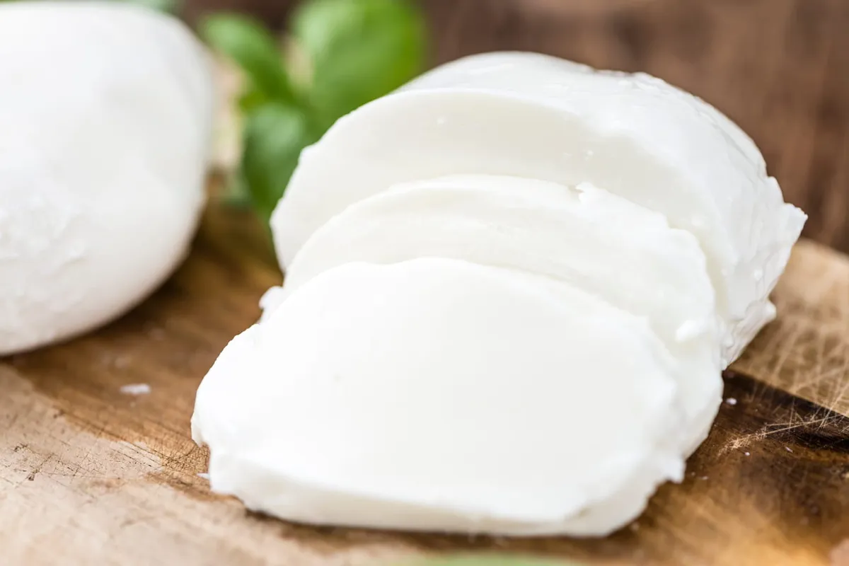 Assiette simple avec tranches de mozzarella fraîche, quelques feuilles de basilic et un rayon de lumière sur un plan de