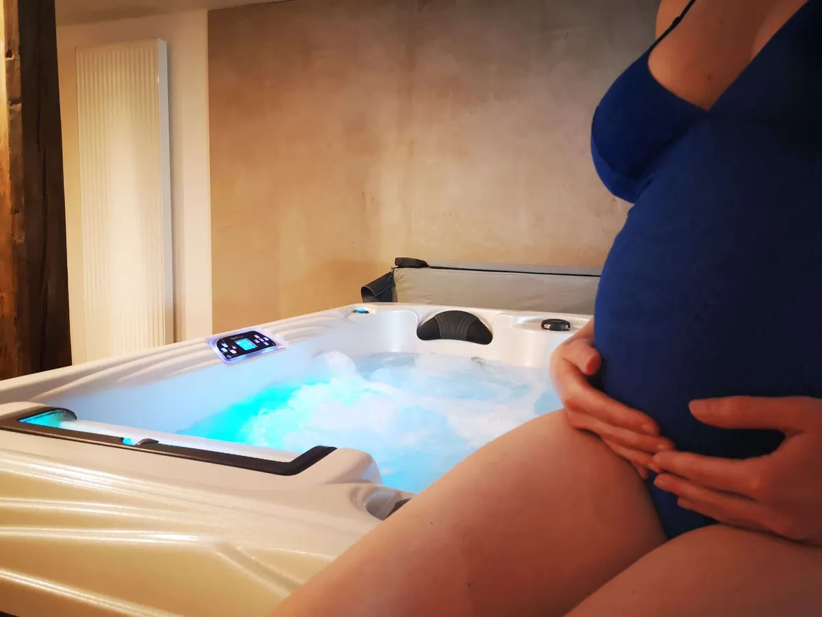 Femme enceinte assise au bord d'un bassin extérieur, les pieds dans l'eau, entourée de végétation