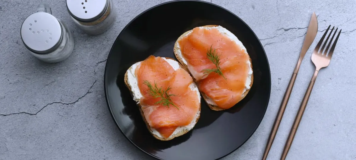 Tranches roses de saumon fumé disposées sur une planche en bois avec rondelles de citron et herbes fraîches